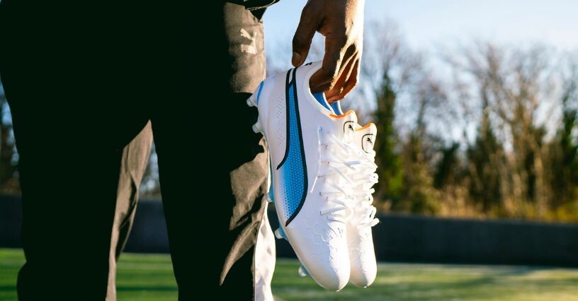 Una persona tiene in mano un paio di scarpe da calcio su un campo