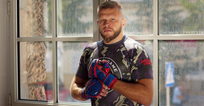 Uomo in abbigliamento MMA con guanti, davanti a una finestra
