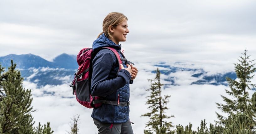 Una persona cammina in montagna indossando una giacca ibrida e uno zaino
