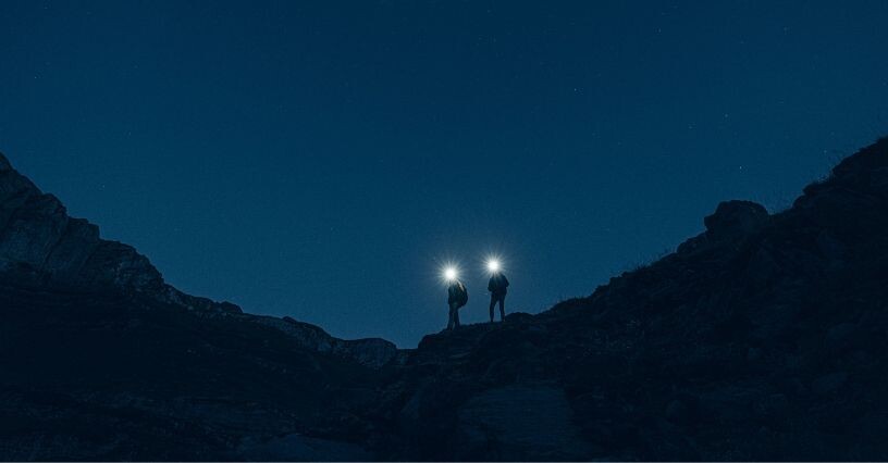 Due persone camminano in montagna di notte con le torce accese
